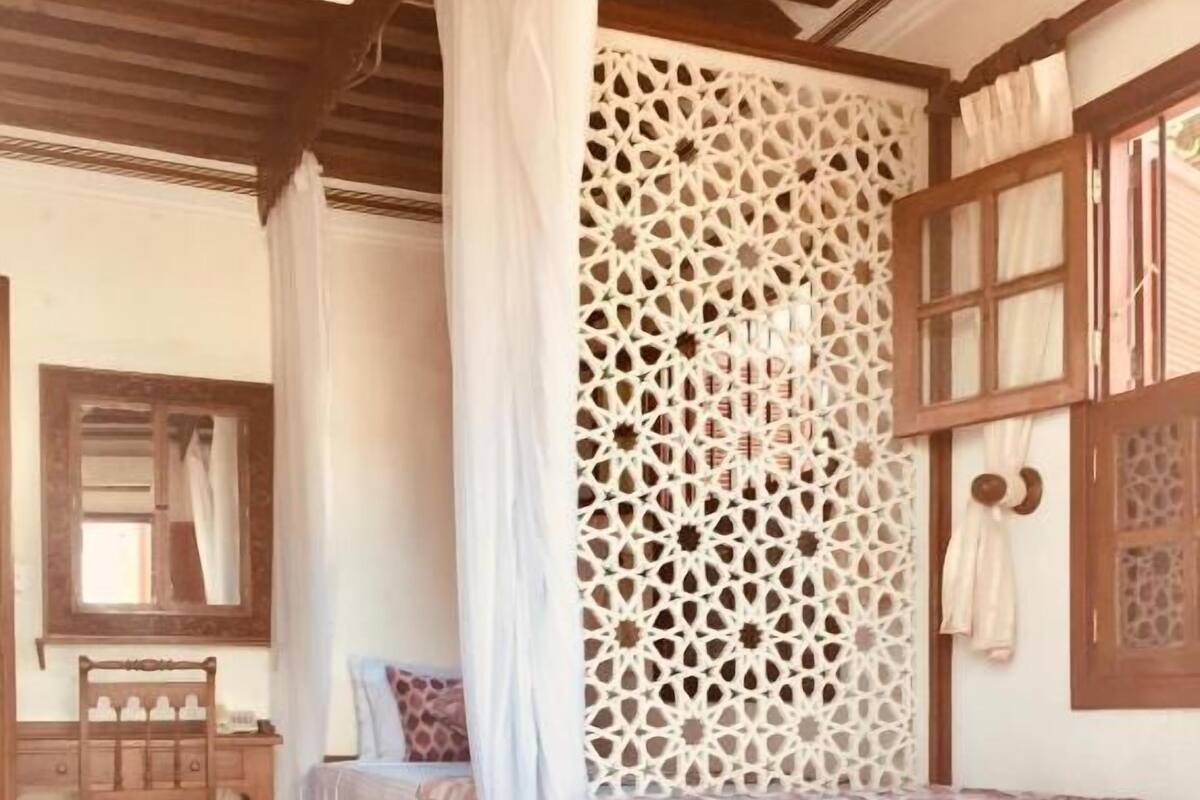 A bedroom with a bed, a wooden desk, a chair, a ceiling fan, and a decorative wall panel.