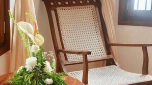 Una silla de madera con respaldo trenzado, una mesa redonda de madera con un centro de flores y una alfombra estampada en el suelo.