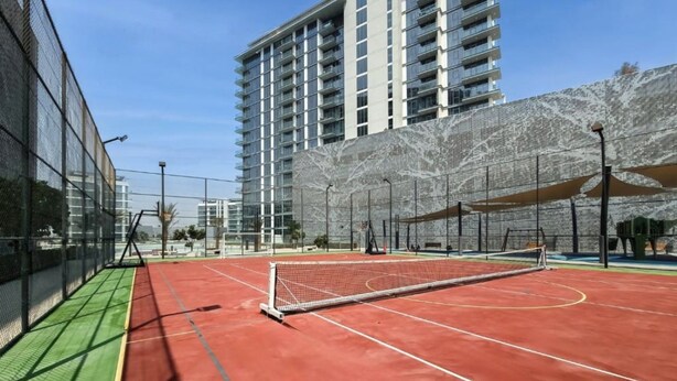 Ein Hallen-Tennisplatz mit Netz, umgeben von einer Umzäunung, und ein Gebäude im Hintergrund.
