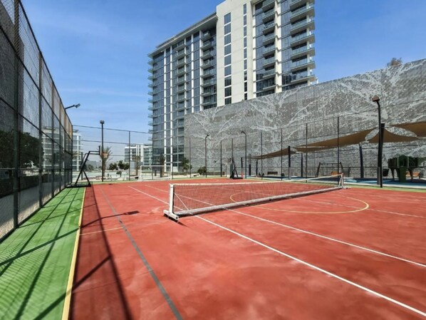 Ein Hallen-Tennisplatz mit Netz, umgeben von einer Umzäunung, und ein Gebäude im Hintergrund.