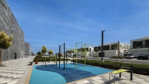 Ein Schwimmbecken mit Trainingsgeräten, ein Schachbrettmuster-Weg und moderne Gebäude im Hintergrund.