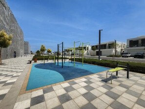 Ein Schwimmbecken mit Trainingsgeräten, ein Schachbrettmuster-Weg und moderne Gebäude im Hintergrund.