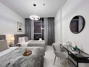 Ein modernes Hotelzimmer mit zwei Betten, einem Schreibtisch, einem Sessel, einem Spiegel und einem Fenster mit Vorhängen.