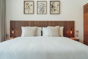 Ein Hotelzimmer mit einem großen Bett, einem hölzernen Kopfteil und drei gerahmten Pflanzenbildern an der Wand.