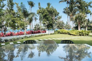 Piscina con agua cristalina que refleja palmeras y un césped cuidado con una zona de estar.