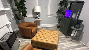 Un salon avec un canapé en cuir marron, un pouf capitonné, une petite table d’appoint avec une lampe, un téléviseur et un meuble.