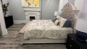 Une chambre à coucher avec un lit, un ventilateur de plafond, une carte du monde accrochée au mur, une cheminée et une fenêtre.
