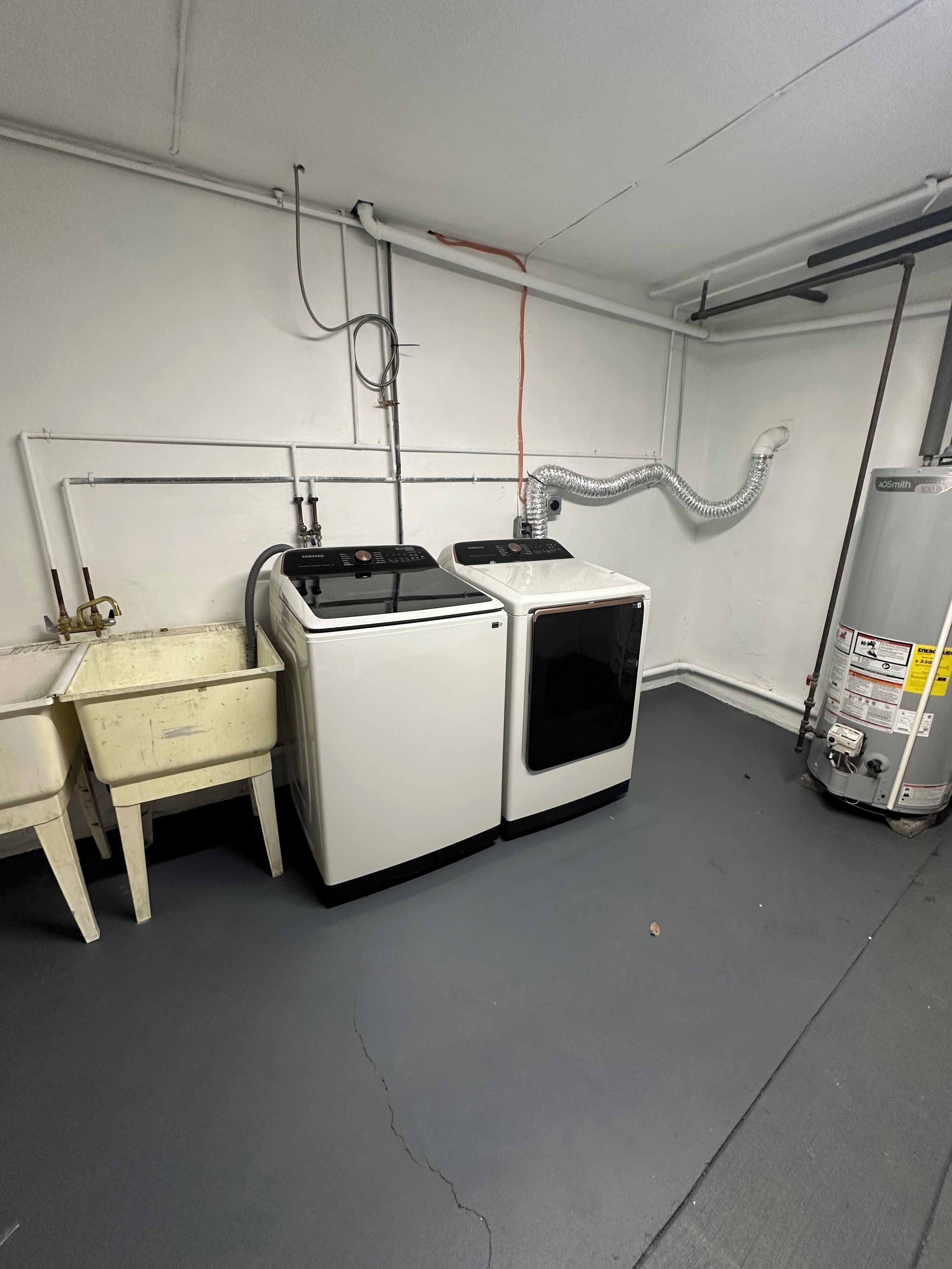 Quarto com máquina de lavar de cor branca, cómoda de madeira pequena e aquecedor de água.