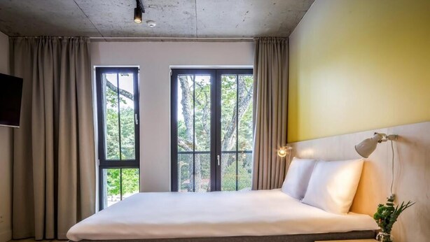 A bedroom with a bed, two windows, a bedside table, and a wall-mounted lamp.