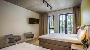 A hotel room with two beds, a TV mounted on the wall, and large windows with curtains.