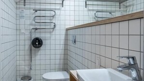 A small, modern bathroom with white tiled walls, a white toilet, a sink with a mirror, and a shower area with a glass enclosure.