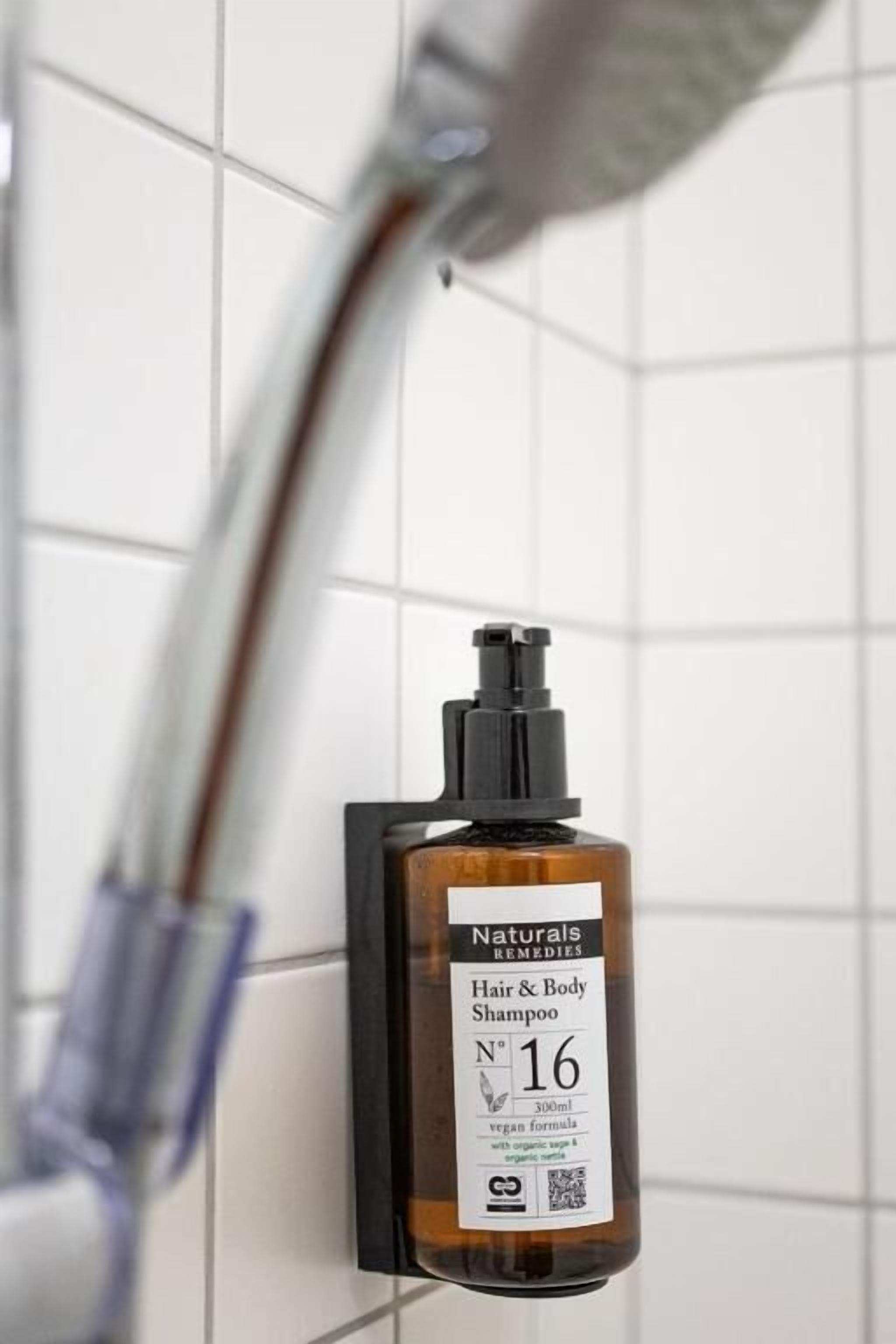 A bottle of Naturals Remedies Hair & Body Shampoo mounted on a tiled wall.