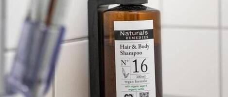 A bottle of Naturals Remedies Hair & Body Shampoo mounted on a tiled wall.