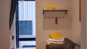 A room with a sofa, a bed with a headboard, a window with curtains, a shelf with towels, and a door leading to another room. - Melt in Palanga Self check-in (Palanga)