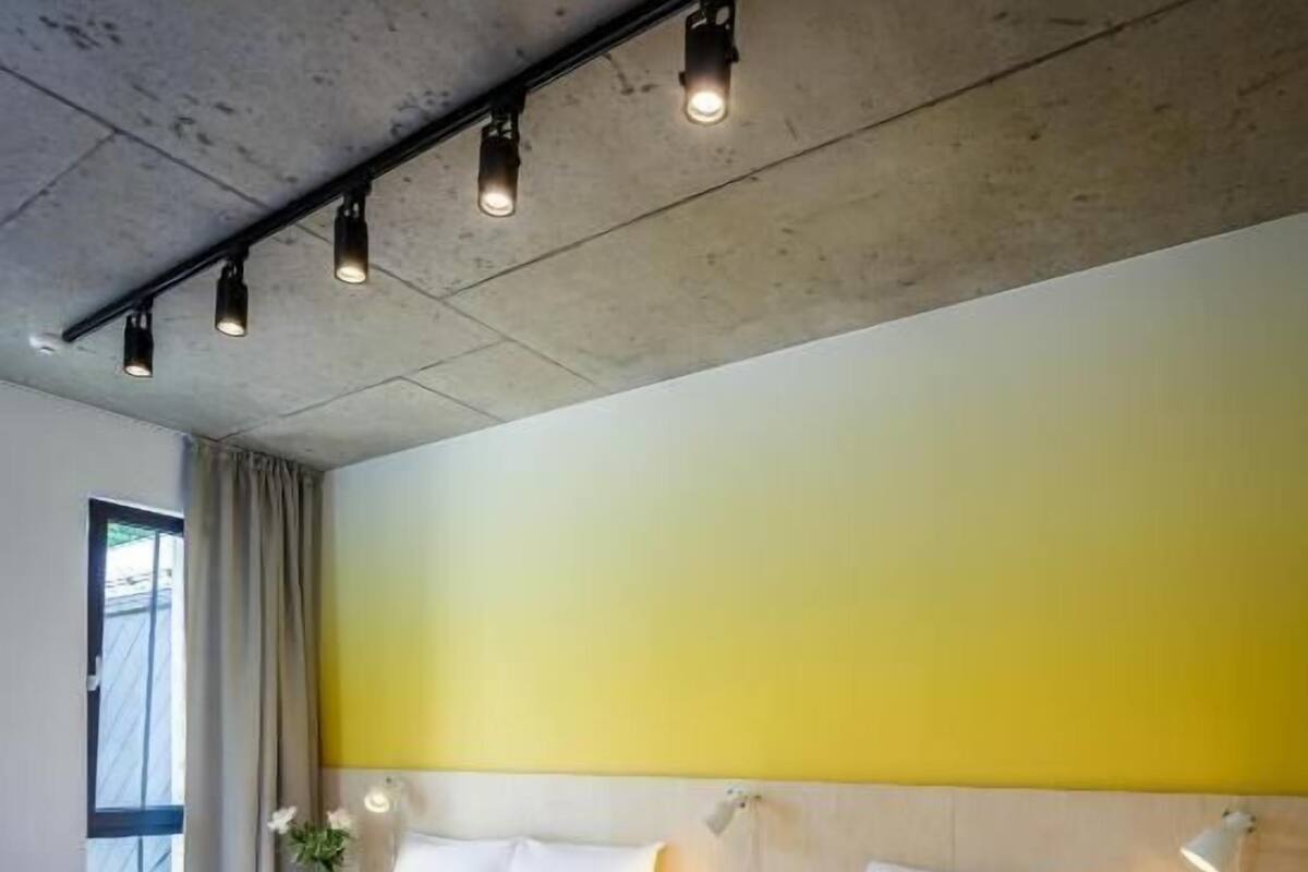 Una habitación de hotel con dos camas, un ventanal con cortinas y una pared amarilla.