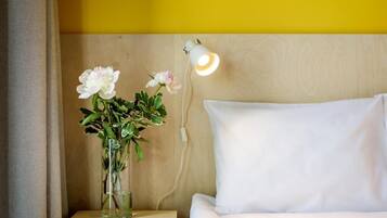 A bed with white bedding, a bedside lamp, and a clear vase with flowers on a wooden nightstand.