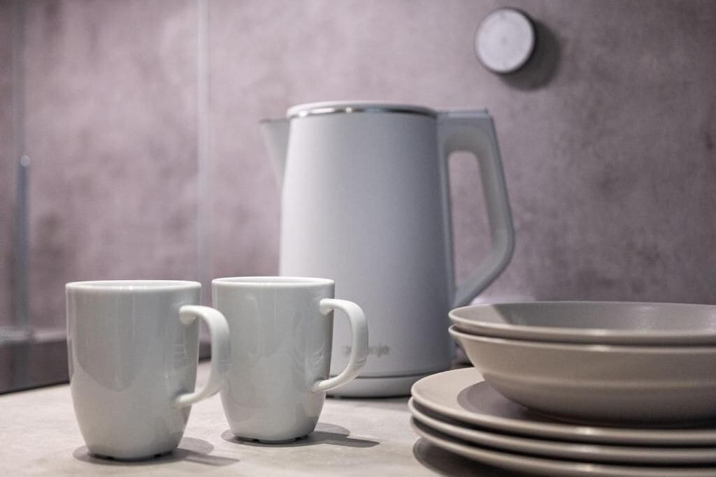 A kitchen with a kettle, two mugs, and stacked plates.