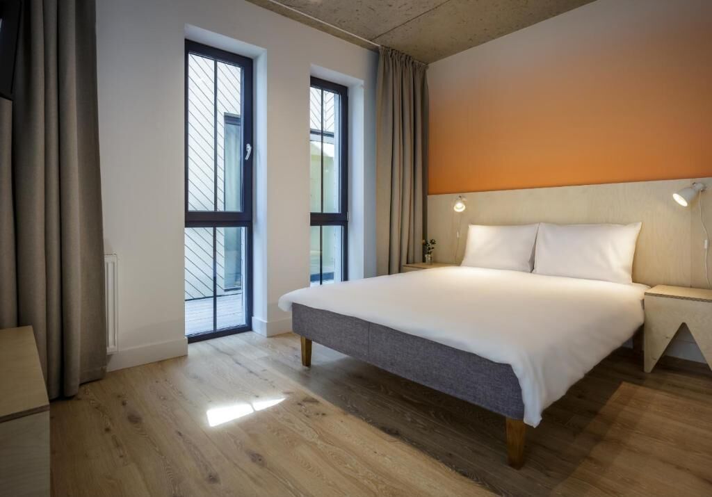 Une chambre d’hôtel moderne avec un grand lit, une table de chevet, une lampe et une vue par la fenêtre.