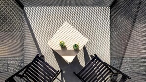 A sunlit outdoor seating area with a table and two chairs, enclosed by a mesh fence.