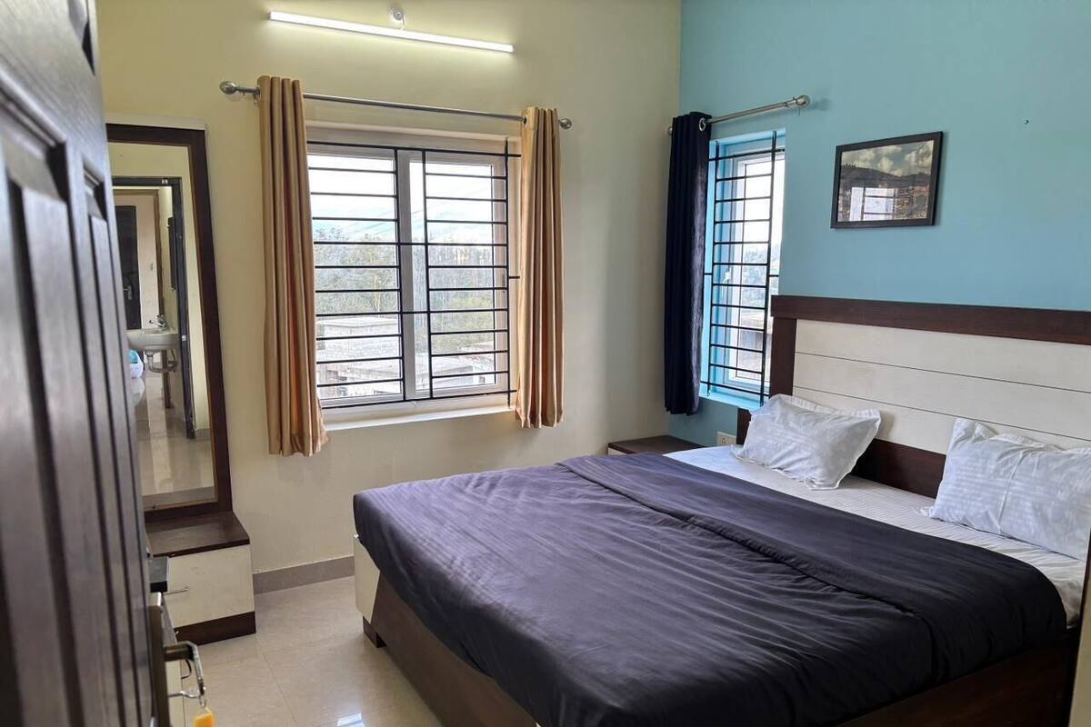 A bedroom with a bed, a window with curtains, a bedside table, and a wall-mounted picture.