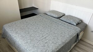 Een bed met een beddekleed met patroon en kussens, een nachtkastje en een radiator.