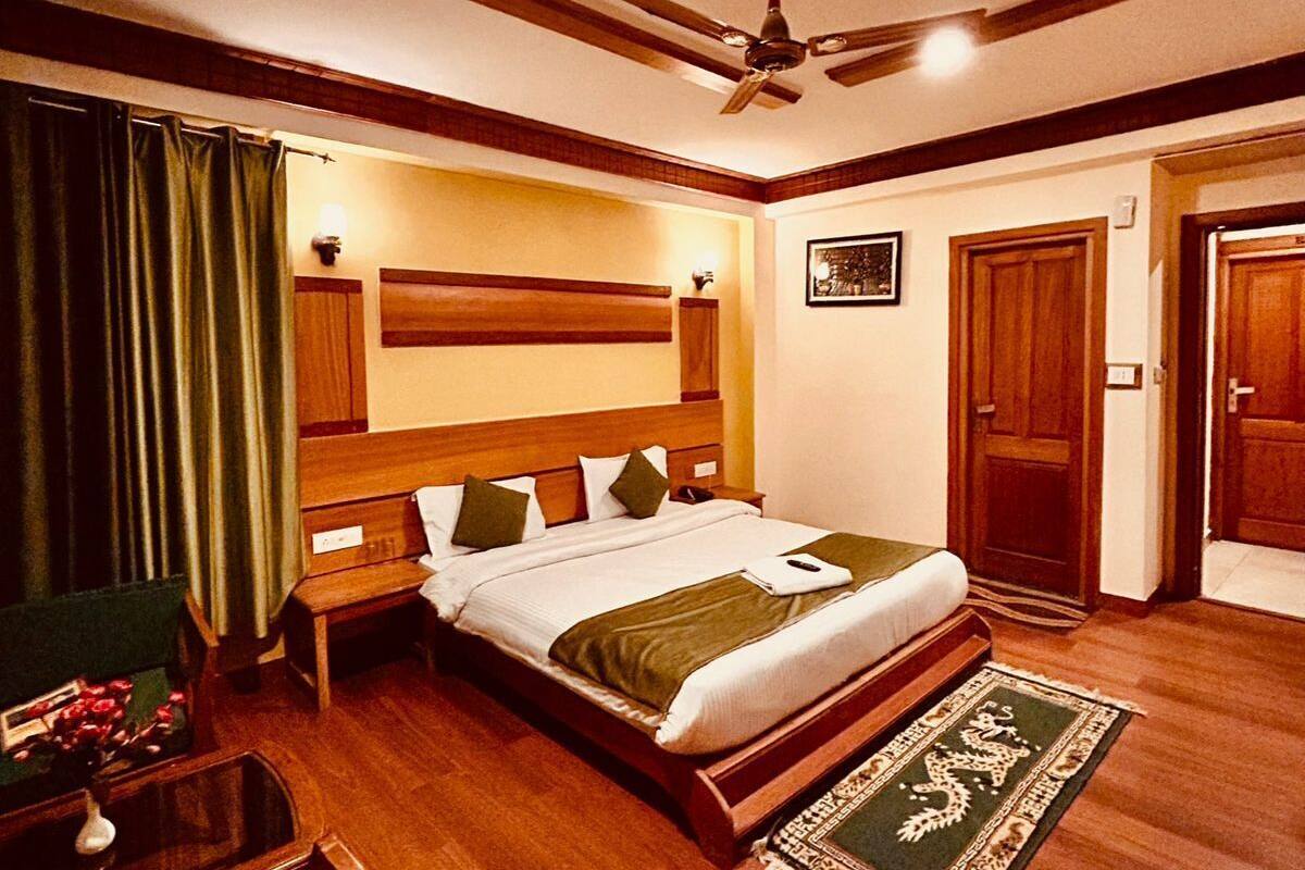 A hotel room with a wooden bed, a ceiling fan, a nightstand, a chair, and a small table with a vase of flowers.