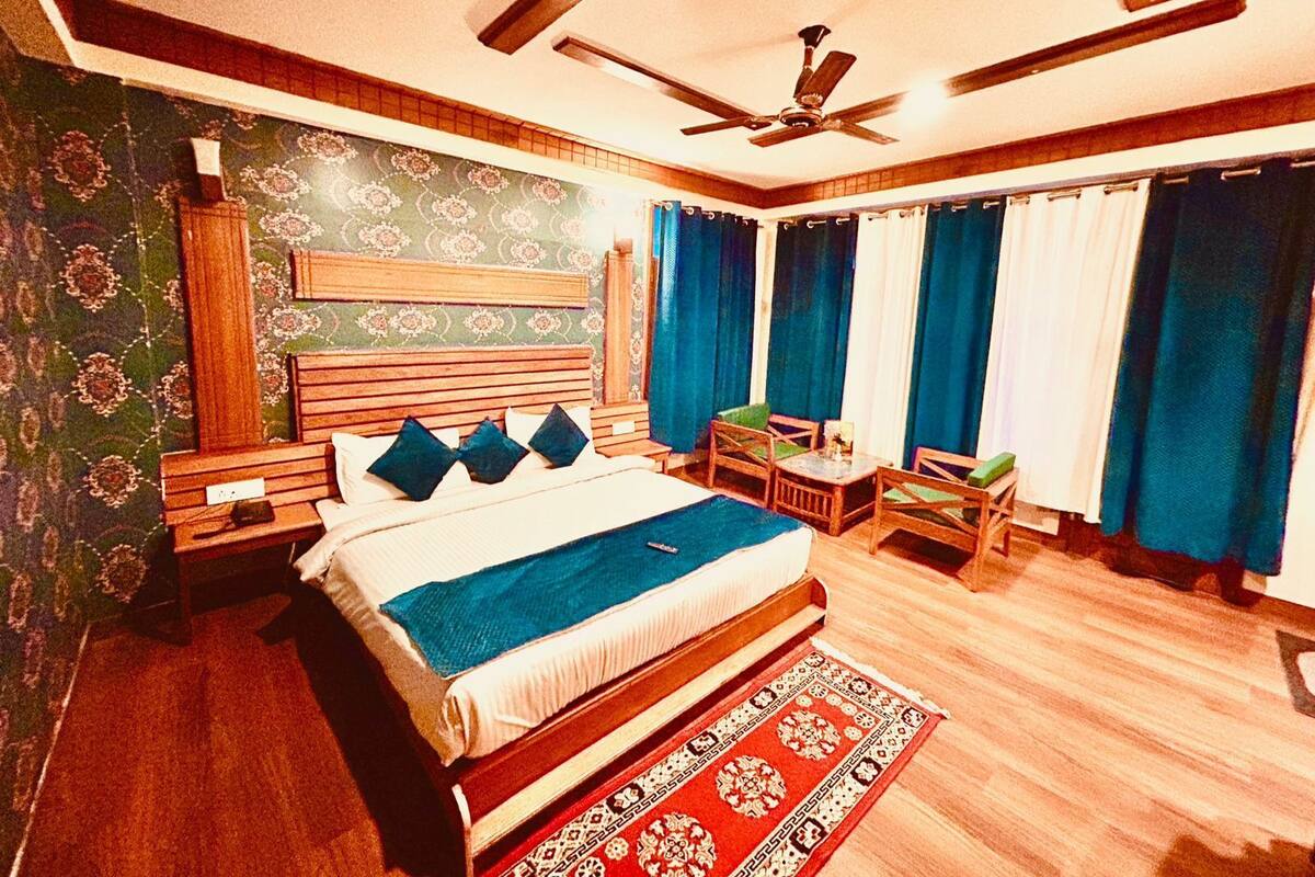 A bedroom with a bed, nightstands, a desk, chairs, a ceiling fan, and curtains.