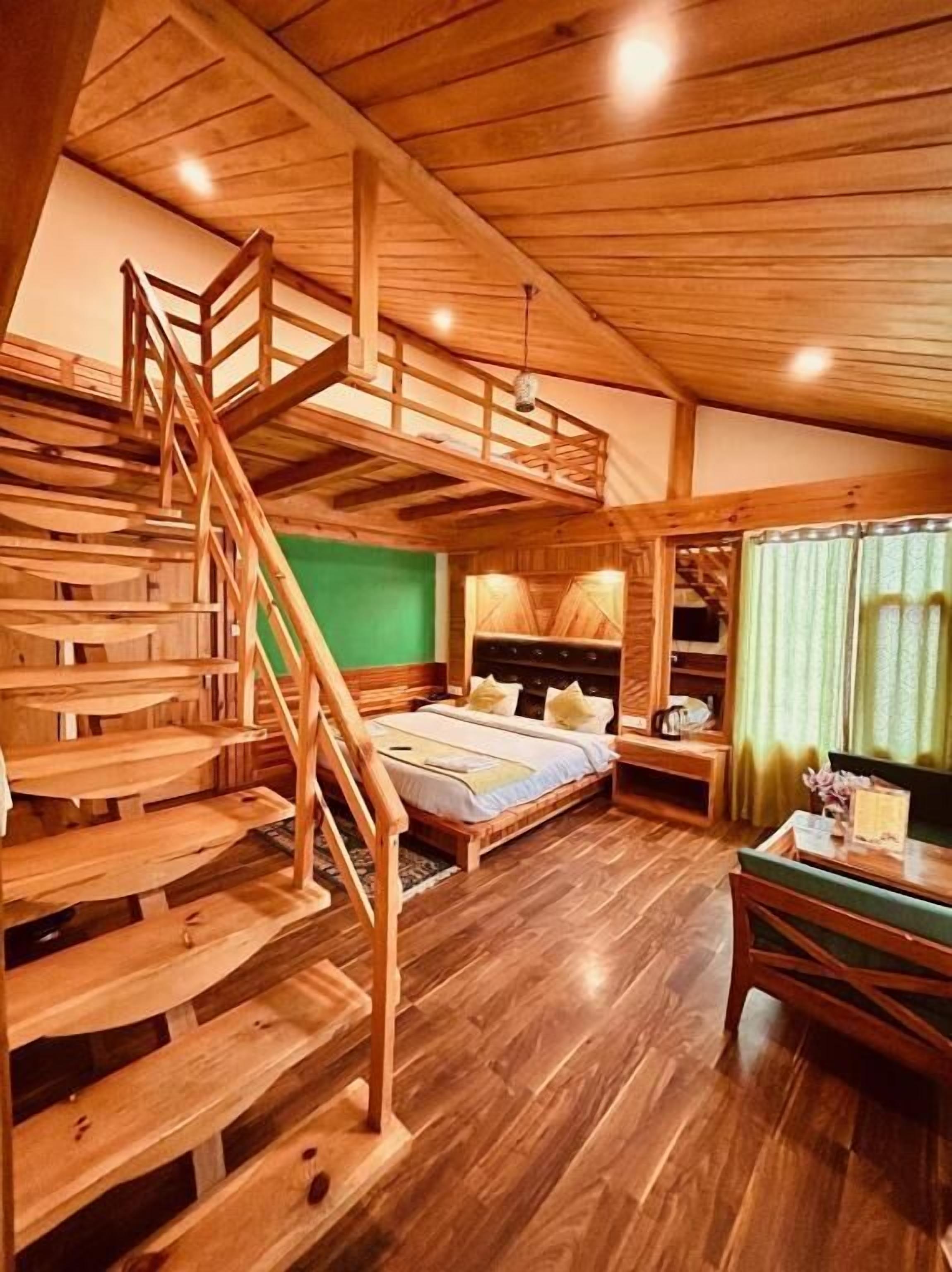 A wooden cabin interior with a loft bed, staircase, and a dining area.