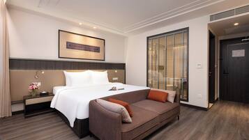 Habitación de hotel con cama, sofá, mesita de noche, una obra de arte en la pared, ventana con persianas y puerta.