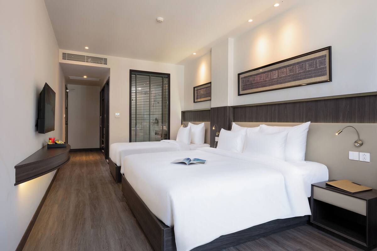 Habitación de hotel con una cama grande, mesitas de noche, un televisor de pantalla plana y una obra de arte enmarcada en la pared.