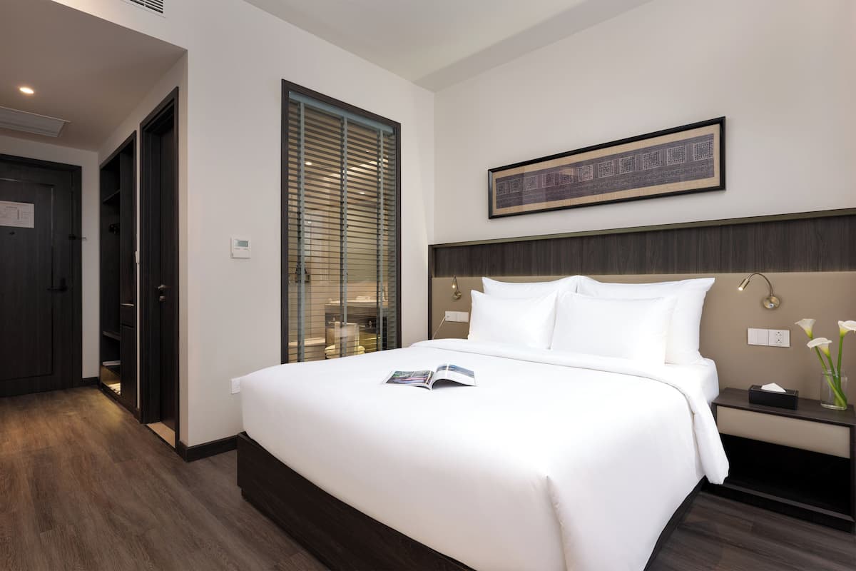 Una habitación de hotel con una cama grande, una mesita de noche con un florero, un cuadro colgado sobre la cama y un vestidor.