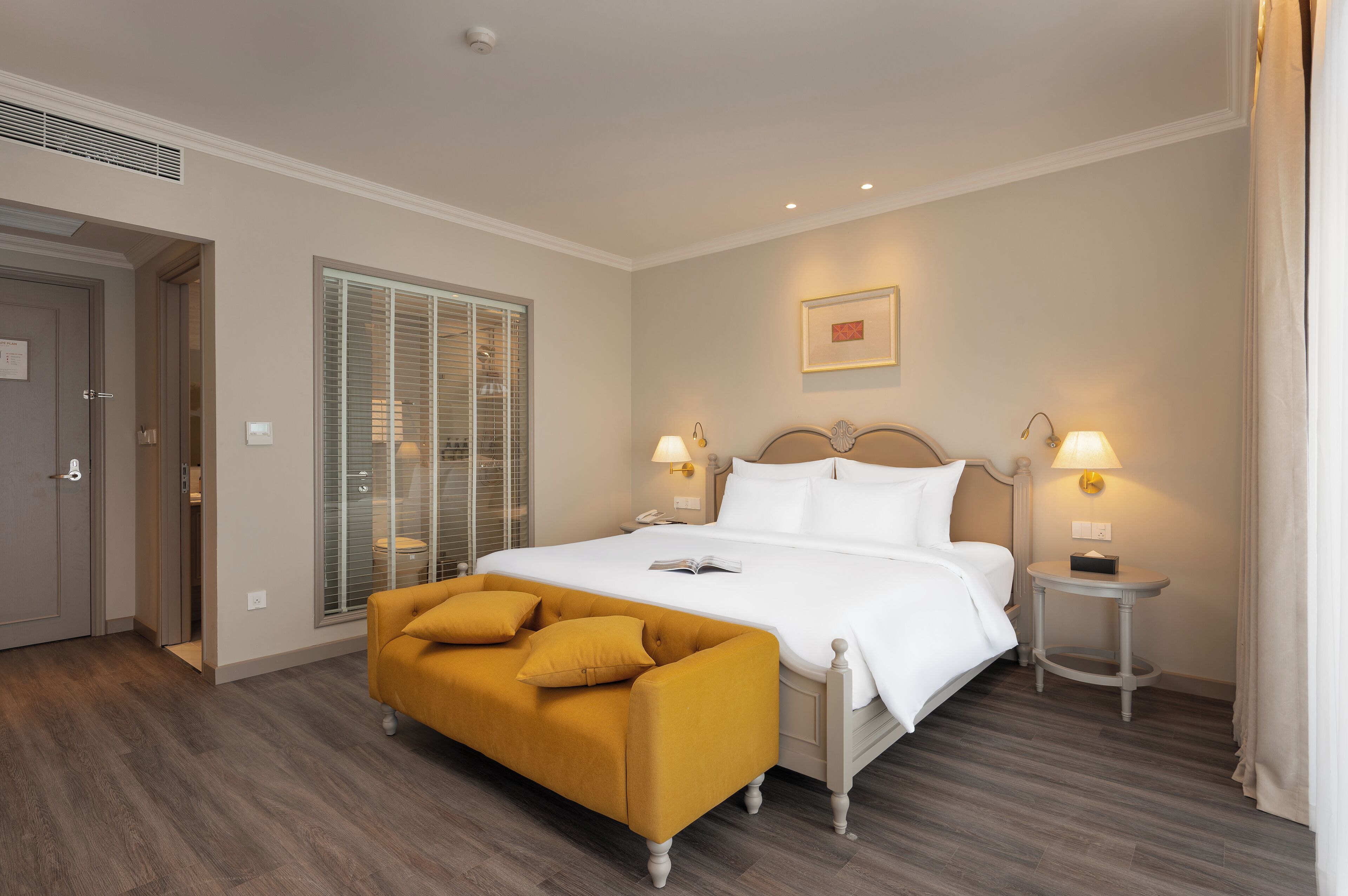 A hotel room with a bed, a small round table, a sofa, and a window with blinds.