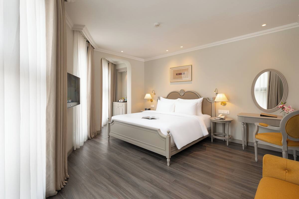 Una habitación de hotel con cama, mesitas de noche, una silla, un espejo y televisión.