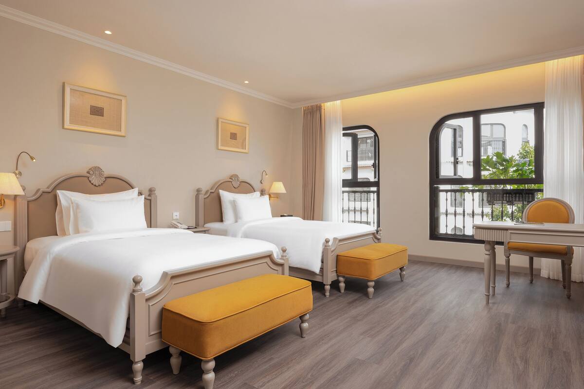 Habitación de hotel con dos camas, un escritorio y una ventana con vistas al exterior.