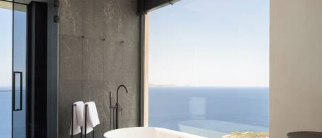 Un baño moderno con una bañera independiente, una ducha a ras de suelo y un amplio ventanal con vistas al mar.