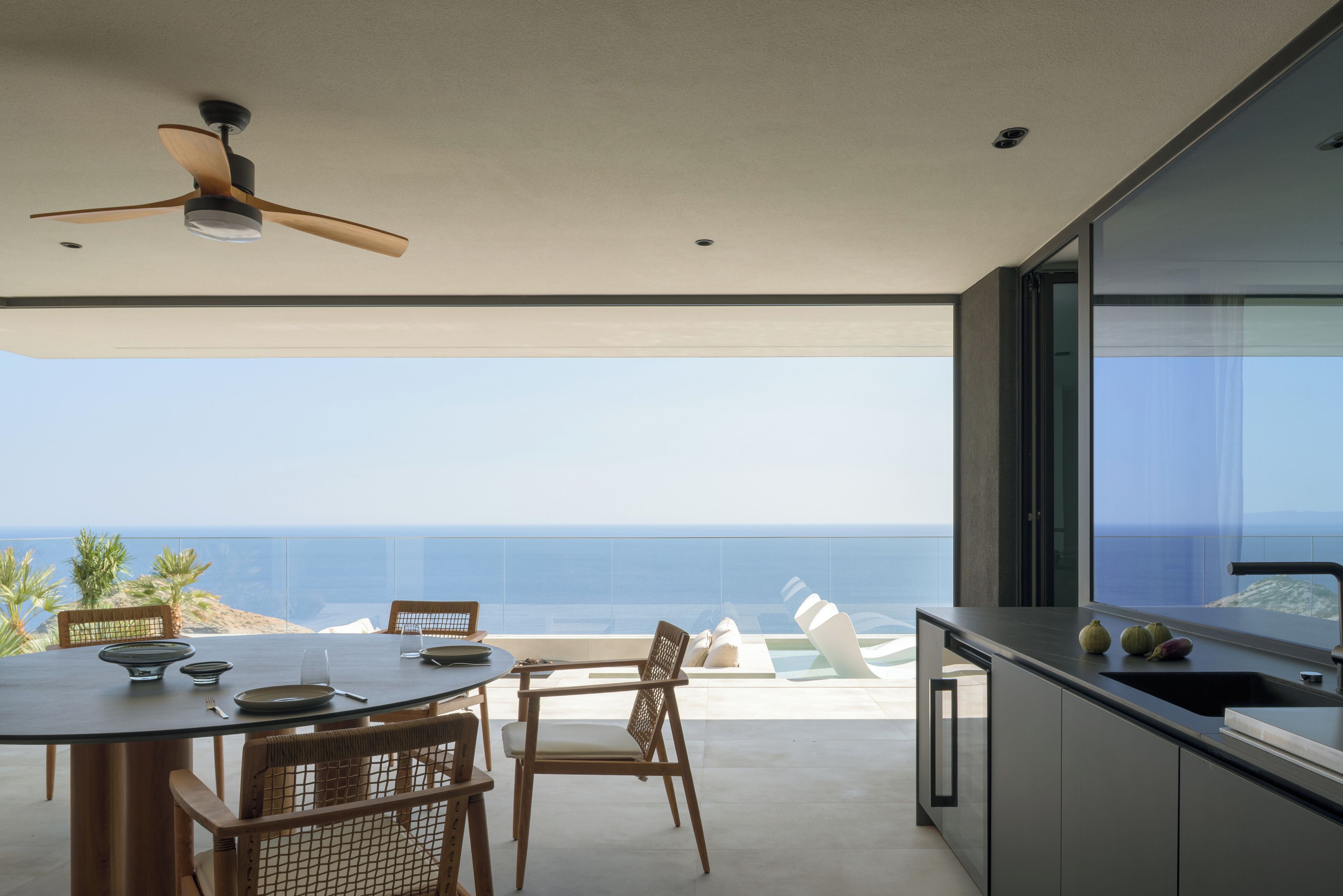 Une cuisine moderne avec vue sur l’océan, un coin repas avec des chaises et un ventilateur de plafond.