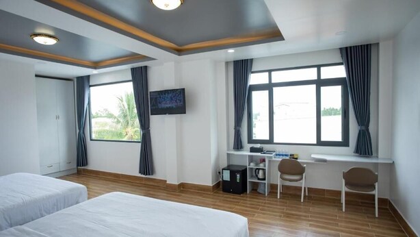 Quarto de hotel com duas camas, uma escrivaninha, uma cadeira, uma televisão e uma janela com cortinas.