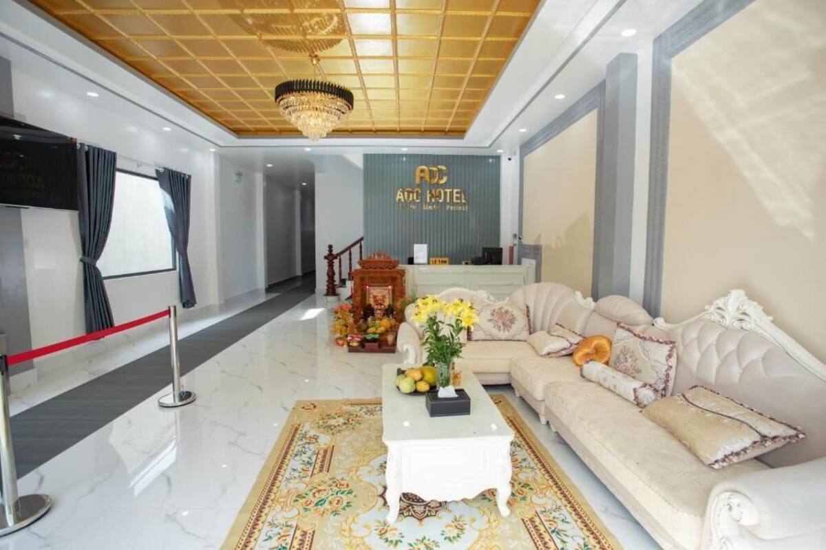 A hotel lobby with a reception desk, a sofa, a coffee table, and a chandelier.