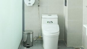 Uma casa de banho moderna com sanita, um contentor de lixo e um porta-toalhas.