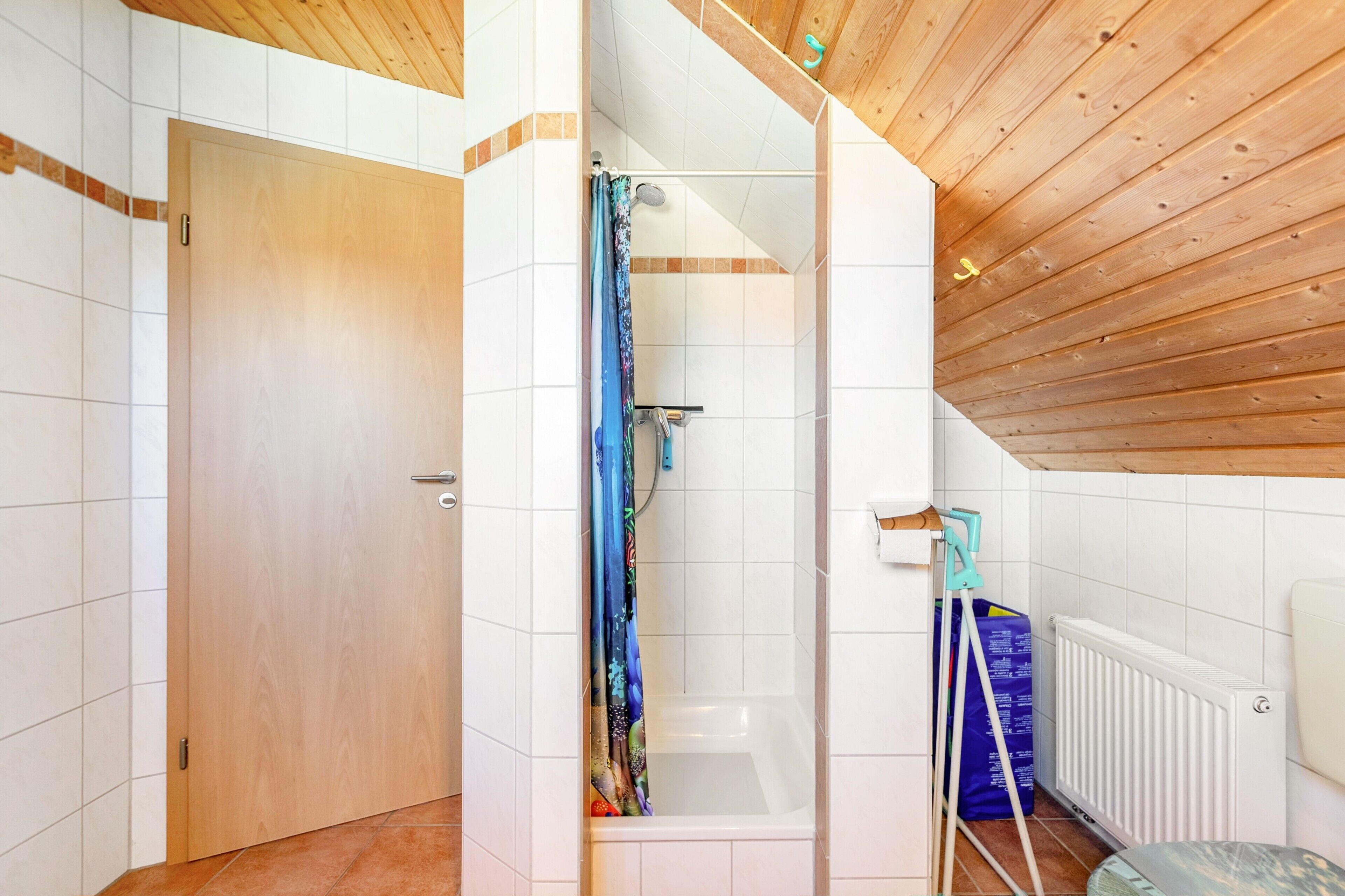 A bathroom with a shower, a bathtub, a wooden ceiling, and a white radiator.