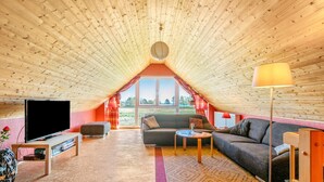 Acogedor dormitorio en ático con televisión, sofá y un amplio ventanal con vistas al exterior.