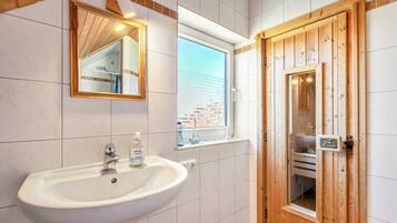 A bathroom with a white sink, a mirror, a window, and a wooden door.