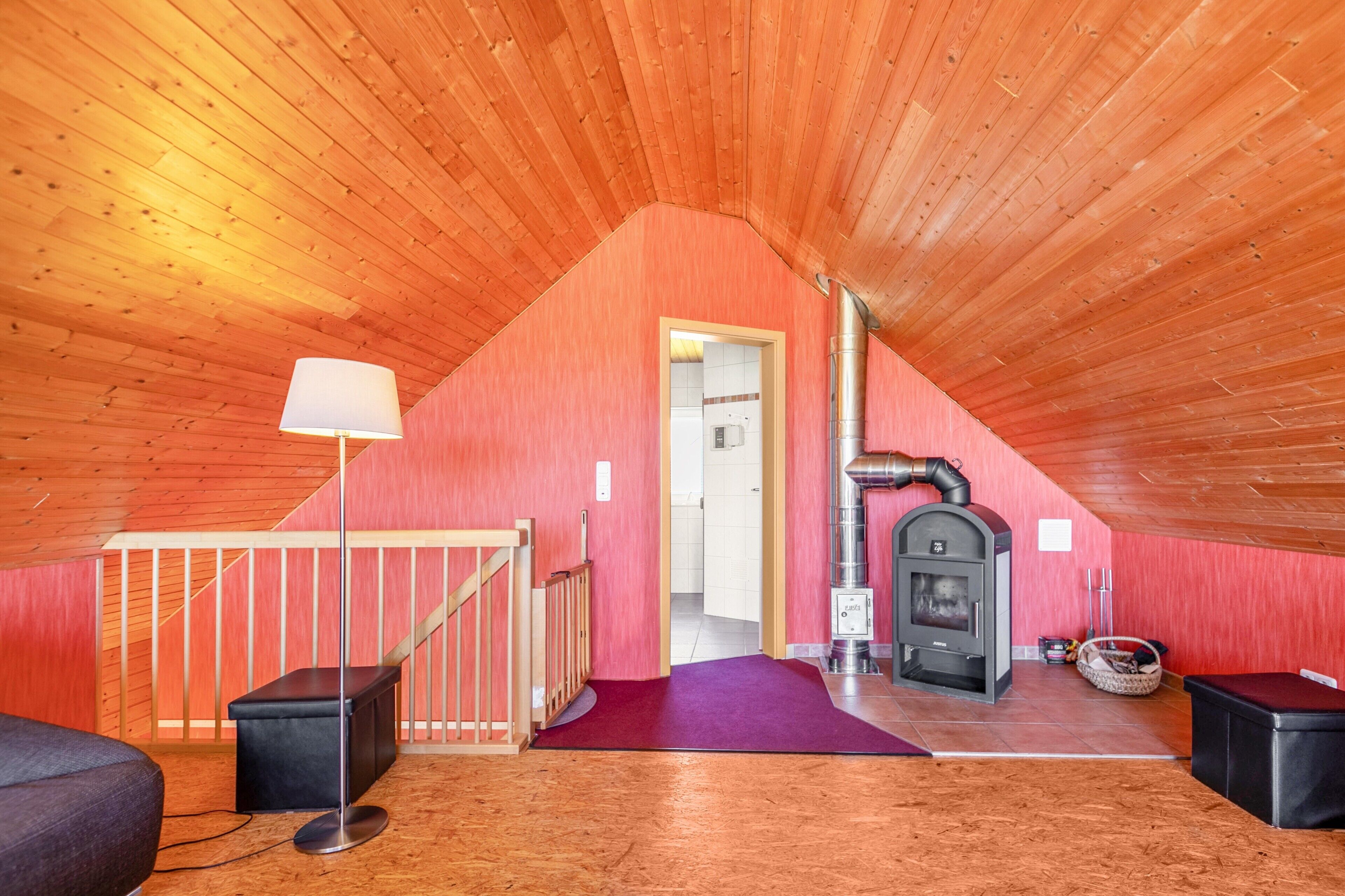 Une pièce mansardée chaleureuse avec un plafond en bois, une cheminée, un escalier et une moquette violette.