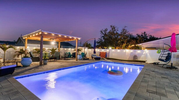 Una piscina con una pergola e un’area relax, circondata da piante in vaso e un recinto bianco.