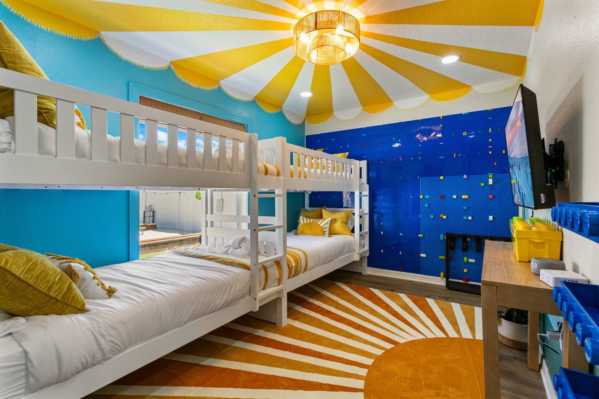 Een kamer met stapelbedden, een blauwe muur met opbergruimte, een houten tafel en een plafondventilator.
