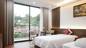 Una habitación de hotel con un amplio ventanal corredero, dos camas, una mesita pequeña y una silla.