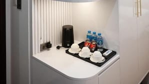 Una estantería blanca curvada con una cafetera, botellas de agua y tazas.