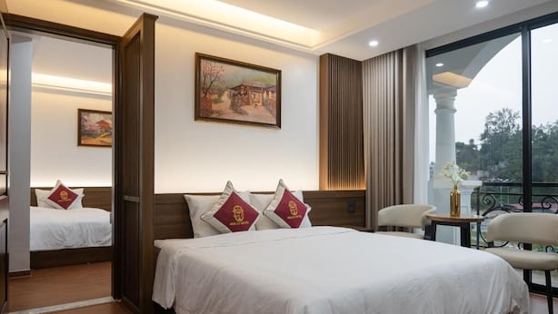Habitación de hotel con una cama grande, dos mesitas de noche, una silla, una mesita pequeña con un florero y un cuadro en la pared.