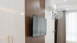 Una habitación de hotel con una cama, un televisor fijado a la pared, un armario y un equipo de aire acondicionado.