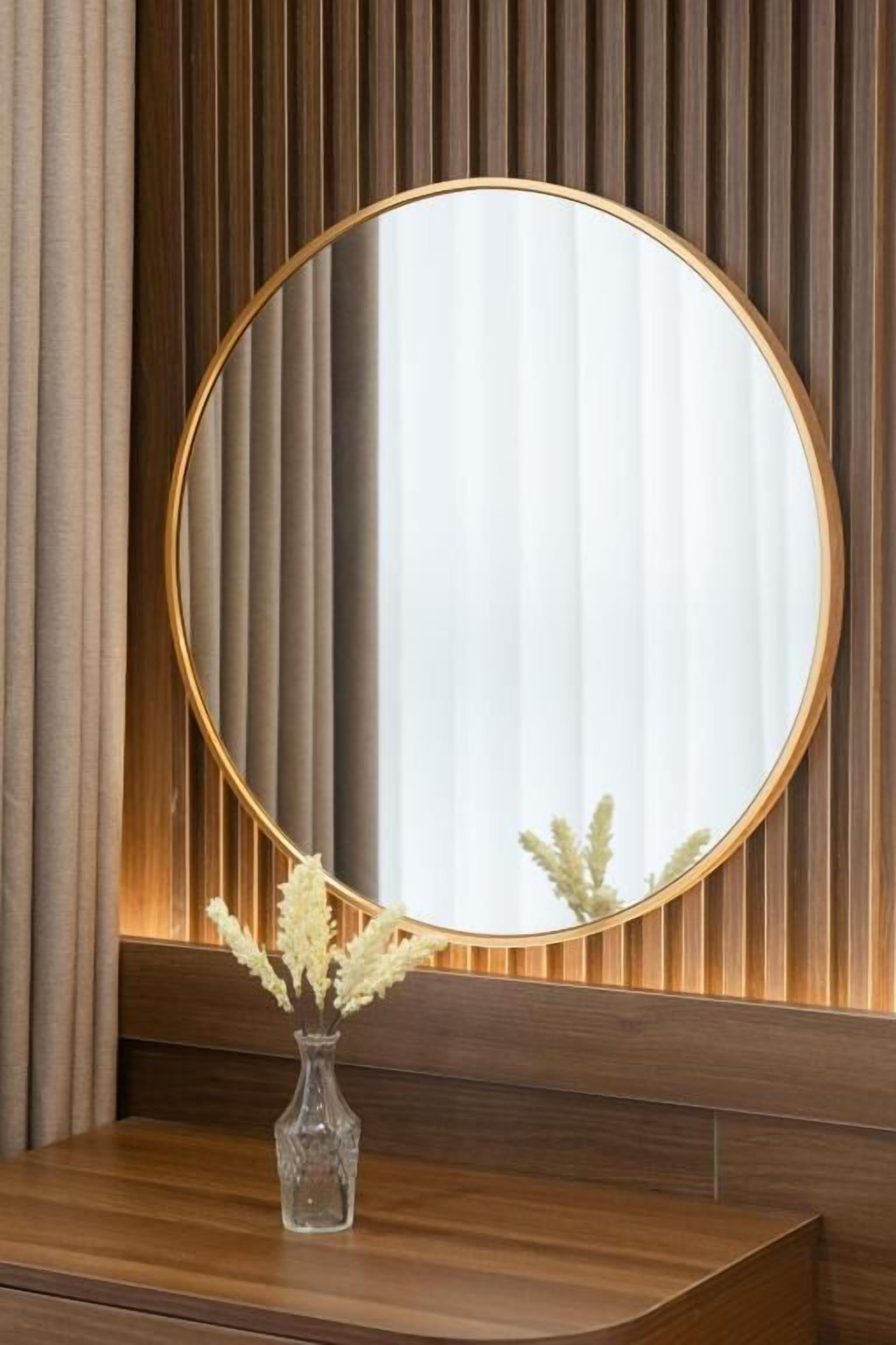 Een ronde spiegel met gouden lijst op een houten wastafelmeubel, tegen een houten wand met verticale latten.